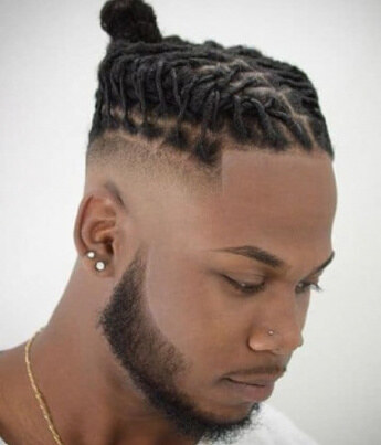 Locs pinned into a top knot over a sharp taper and beard line